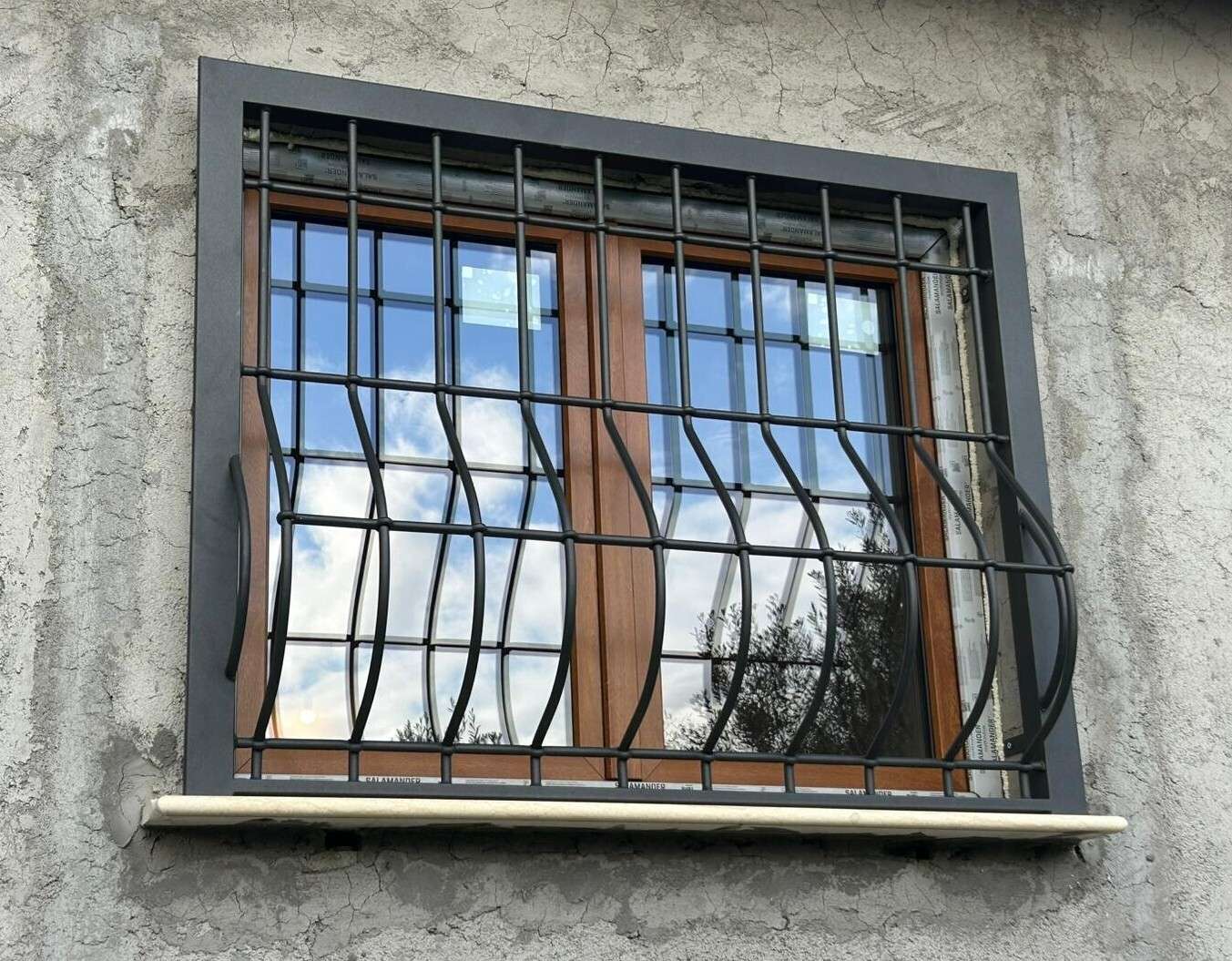 Finestra in legno protetta da una grata ondulata antracite su una facciata in intonaco grezzo