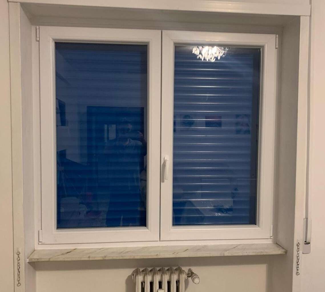 Finestra in PVC bianco a due ante con tapparella blu abbassata, vista dall’interno