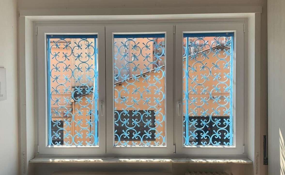 Finestra in PVC bianco a tre ante con grate decorative azzurre all’esterno