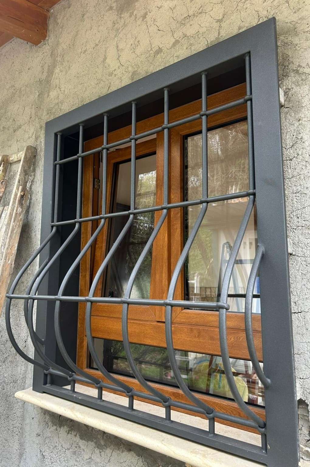 Grata di sicurezza antracite con barre ondulate davanti a una finestra in legno