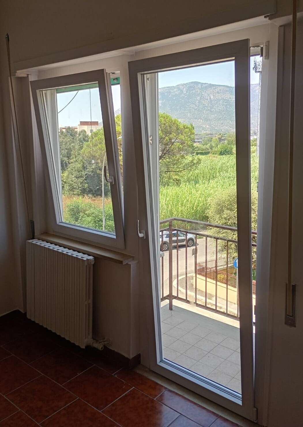 Portafinestra in PVC bianco aperta su un balcone, con i monti sullo sfondo