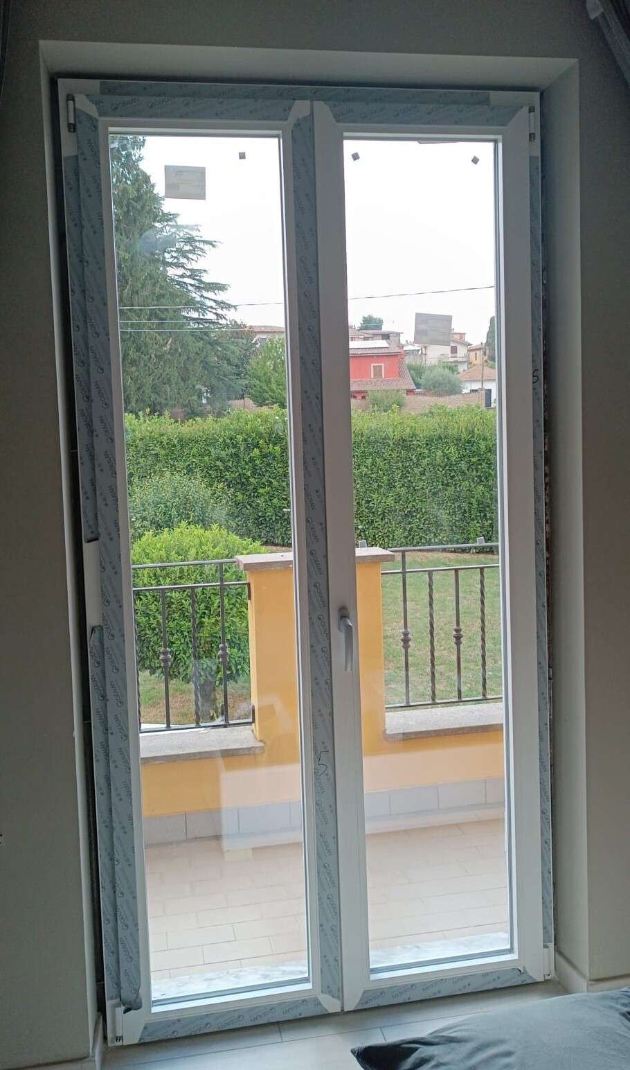 Portafinestra in PVC bianco a due ante affacciata su un giardino con siepe