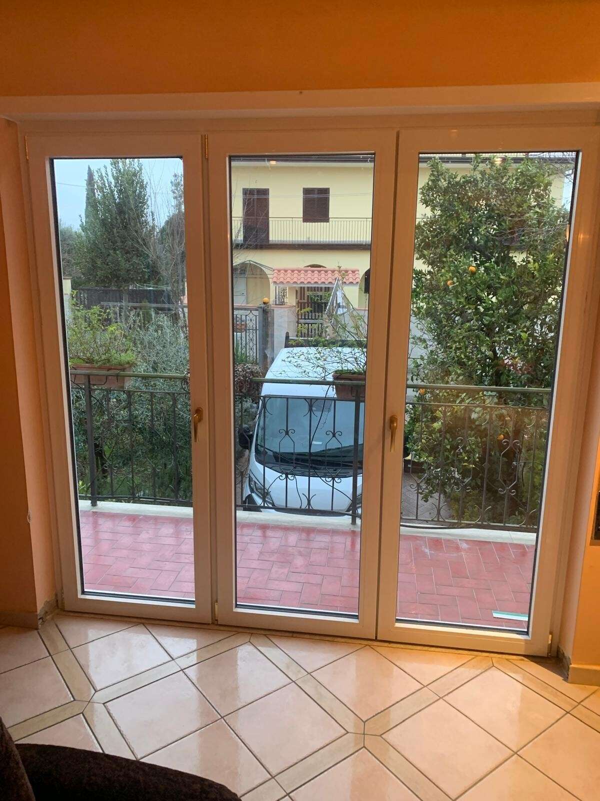 Portafinestra bianca a tre ante che si affaccia su un terrazzo con vista sul giardino